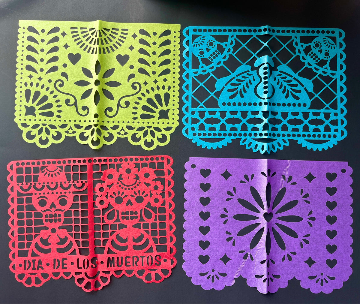 Four colorful papel picado flags with intricate patterns on a black background