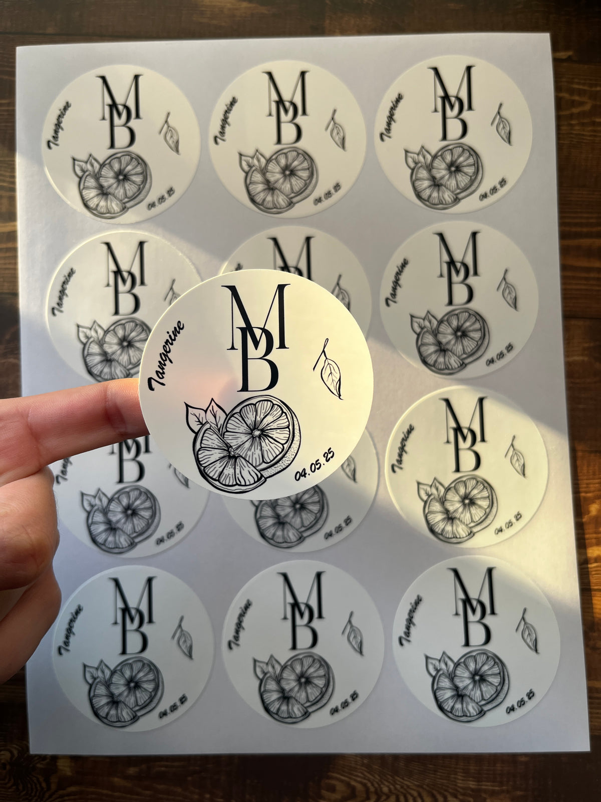 Sheet of round stickers with a monogram design on a wooden surface.