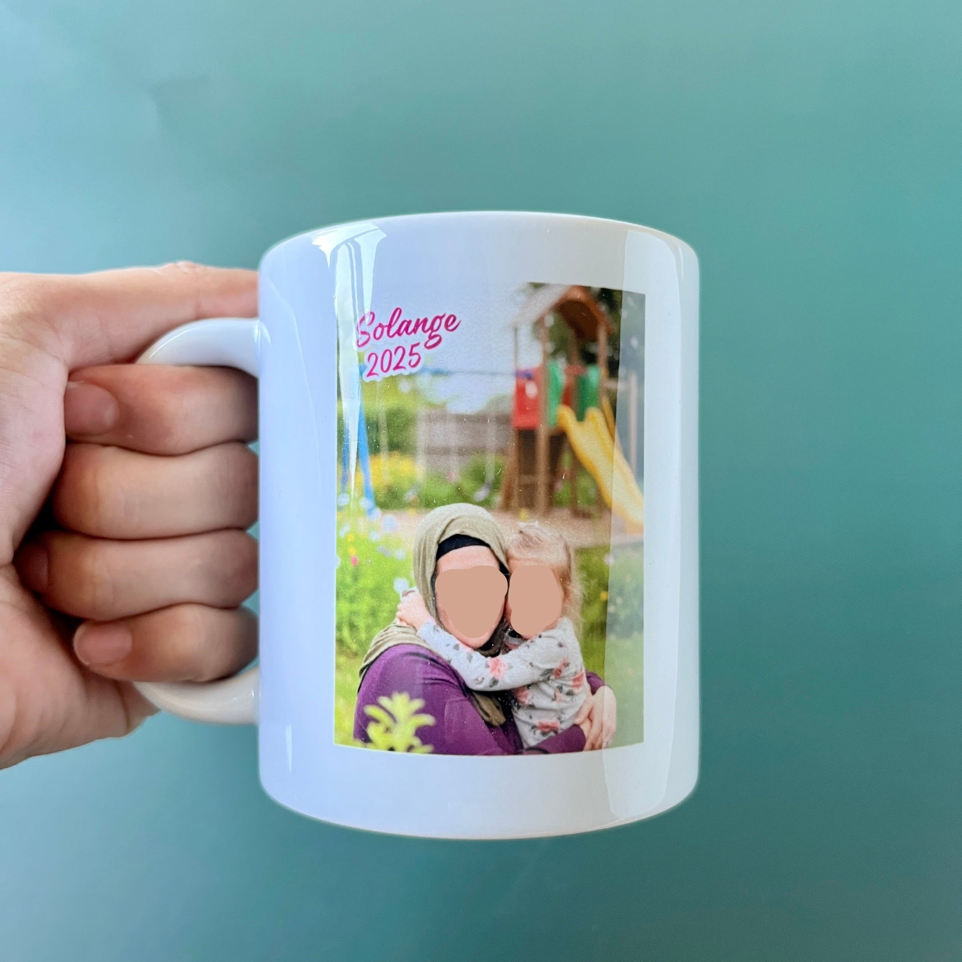 Hand holding a white mug with a photo of a woman and child on a light blue background