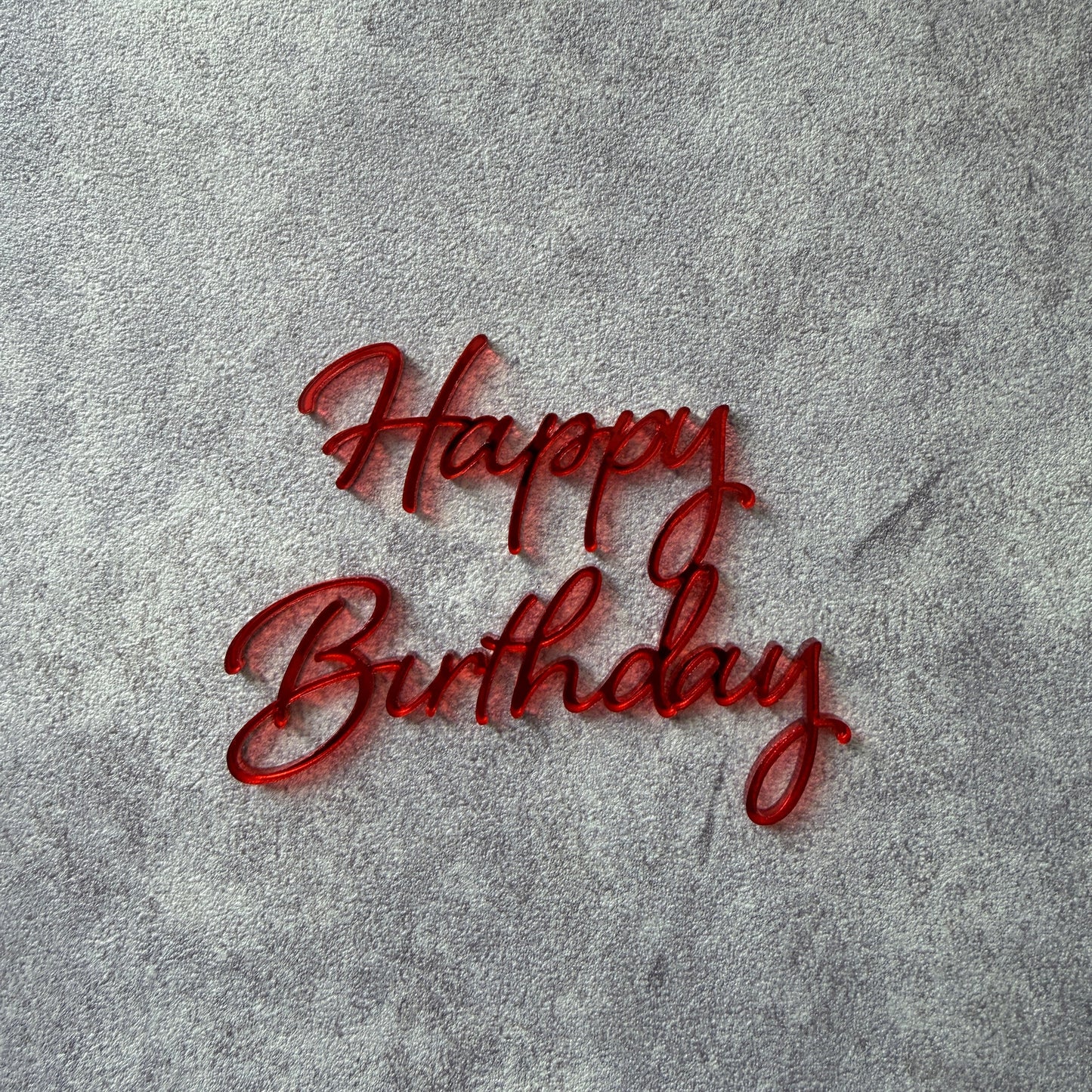 Red 'Happy Birthday' cake topper on a textured gray background