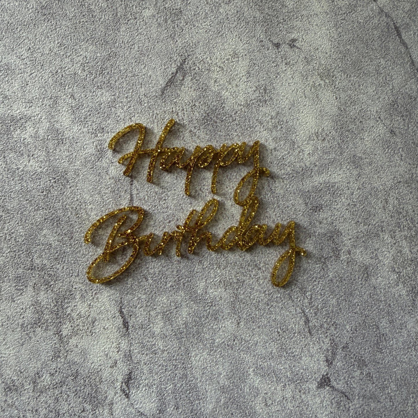 Gold glittery cake topper on a textured gray surface
