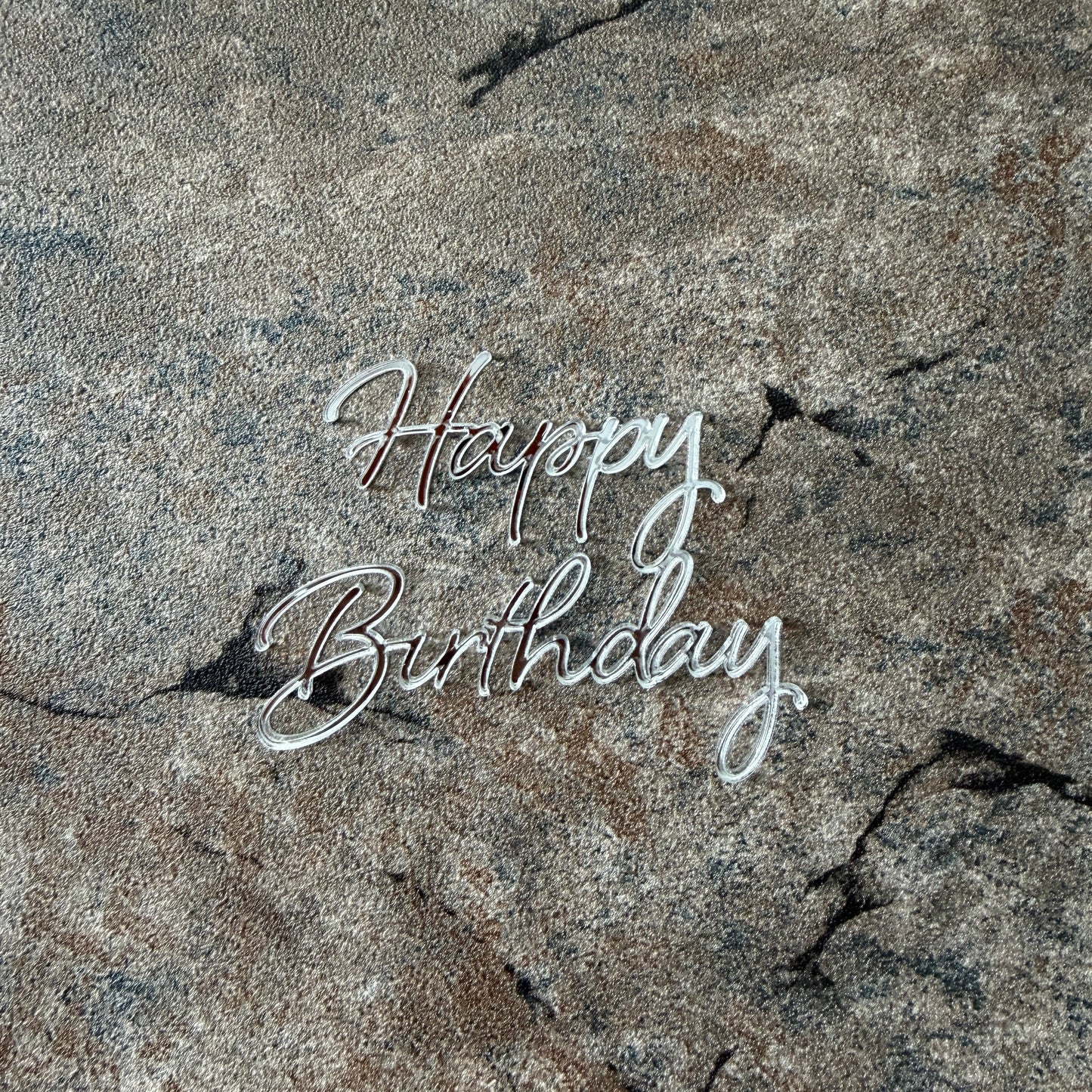 cake topper 'Happy Birthday' on a rock surface