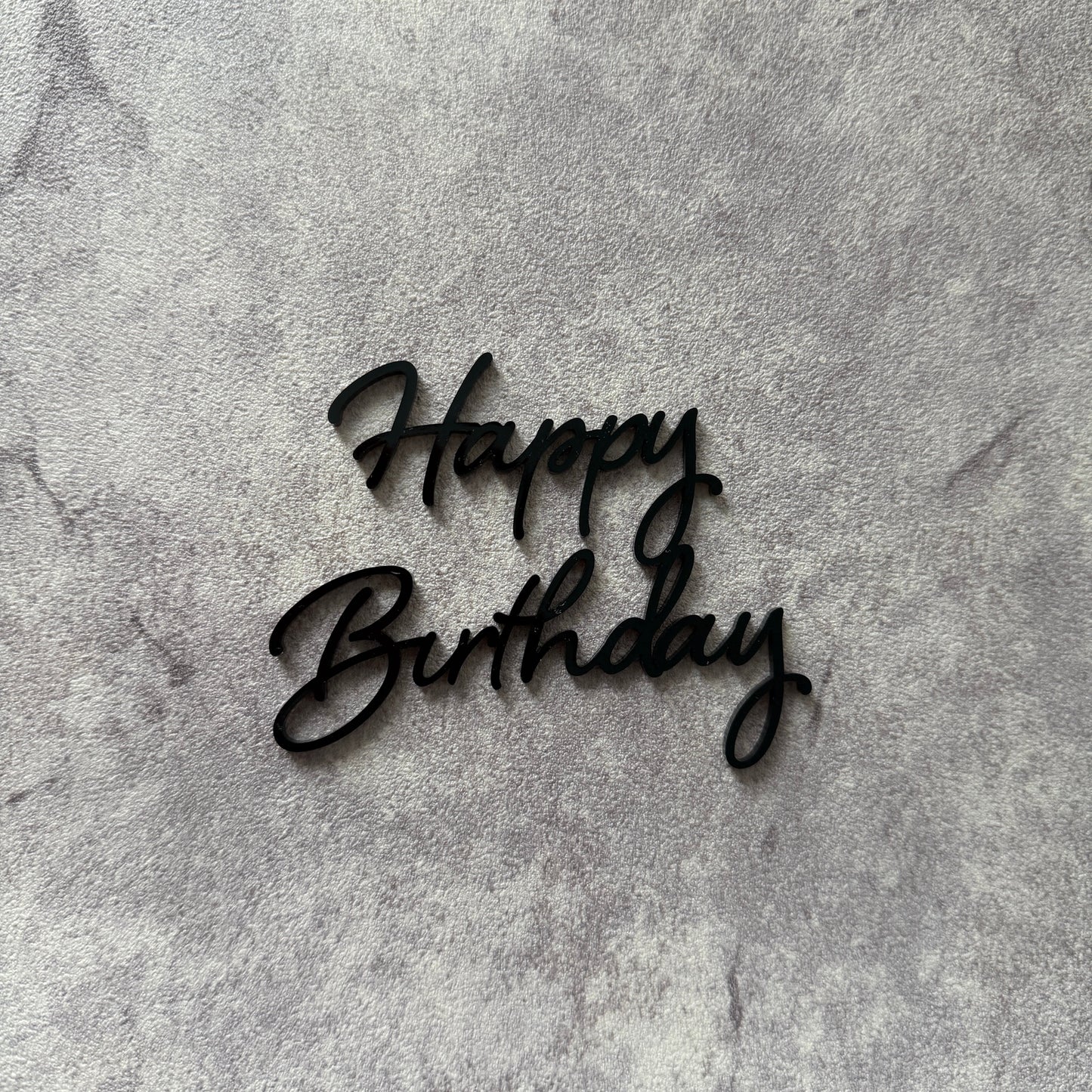 Black 'Happy Birthday' cake topper on a textured gray background