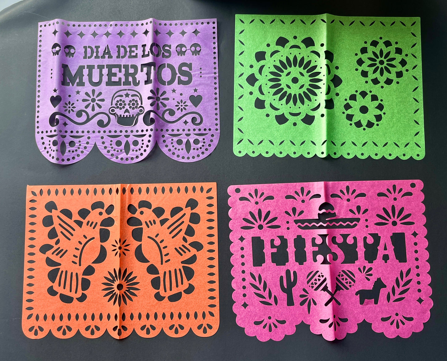 Four colorful papel picado flags with different designs on a dark background