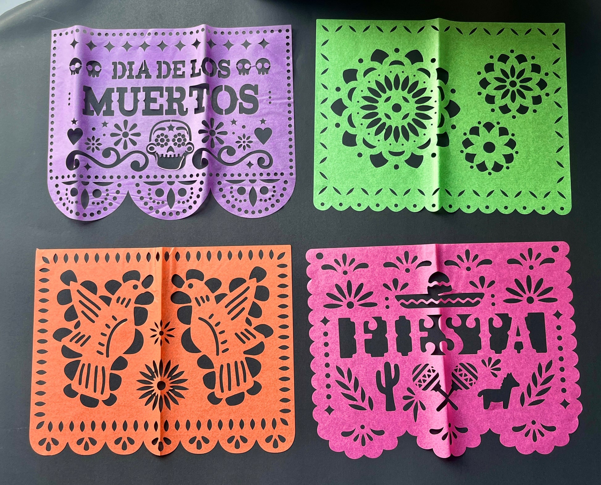 Four colorful papel picado flags with different designs on a dark background