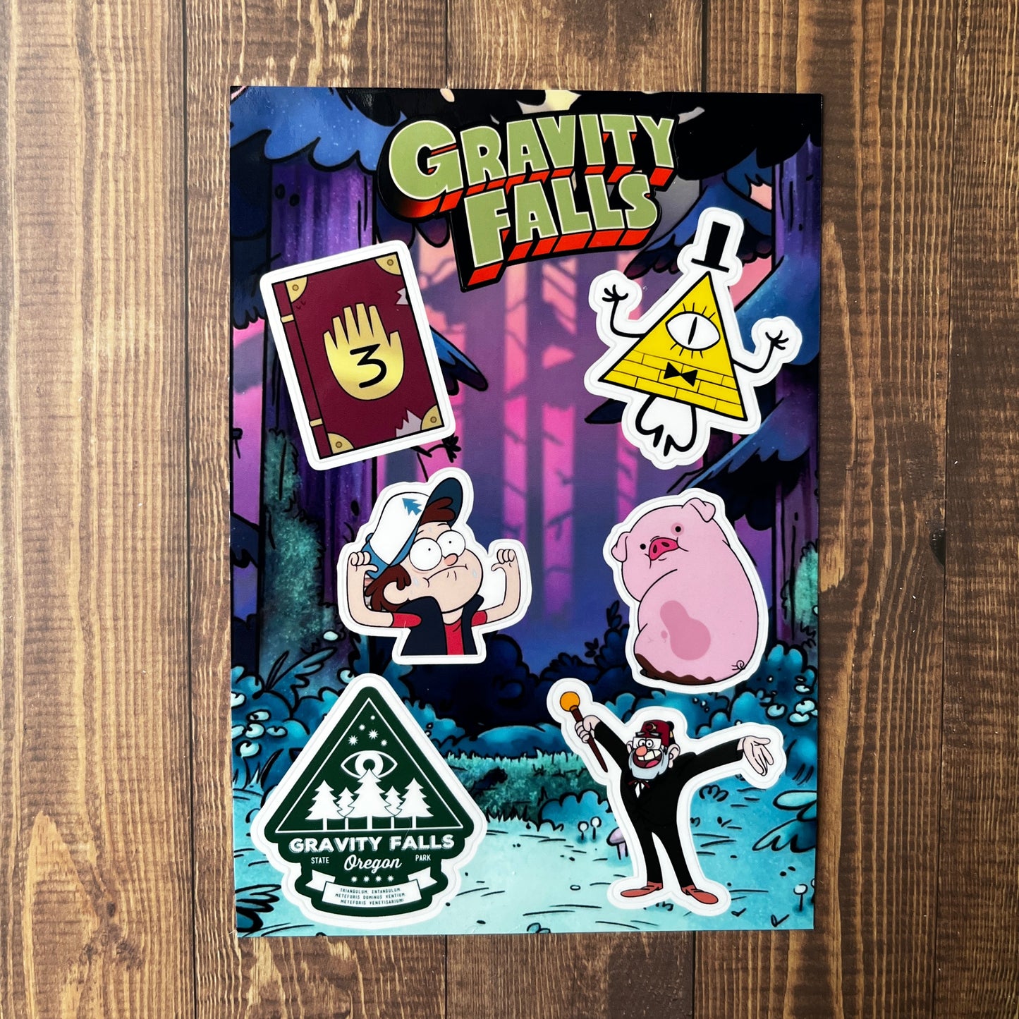 Sticker sheet with 'Gravity Falls' characters and logo on a wooden surface