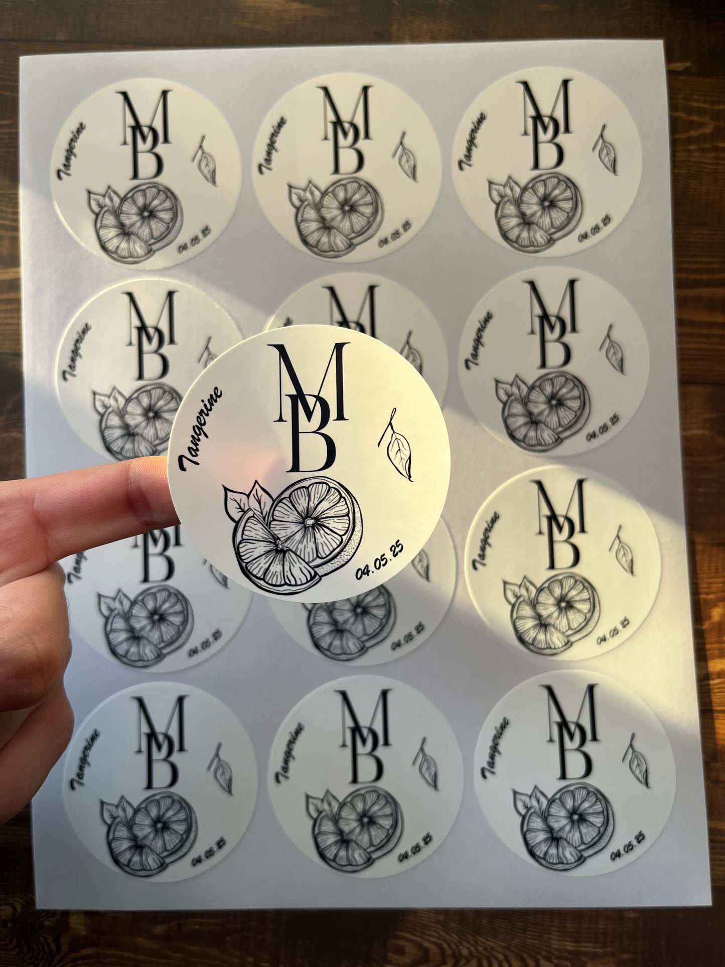 Sheet of round stickers with a monogram design on a wooden surface.