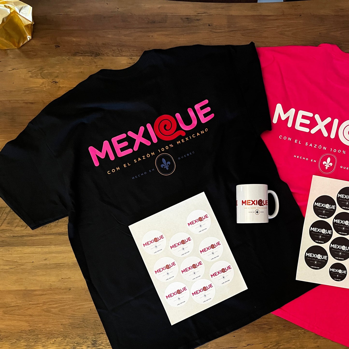 Black and pink t-shirts with 'MEXIQUE' branding on a wooden surface.