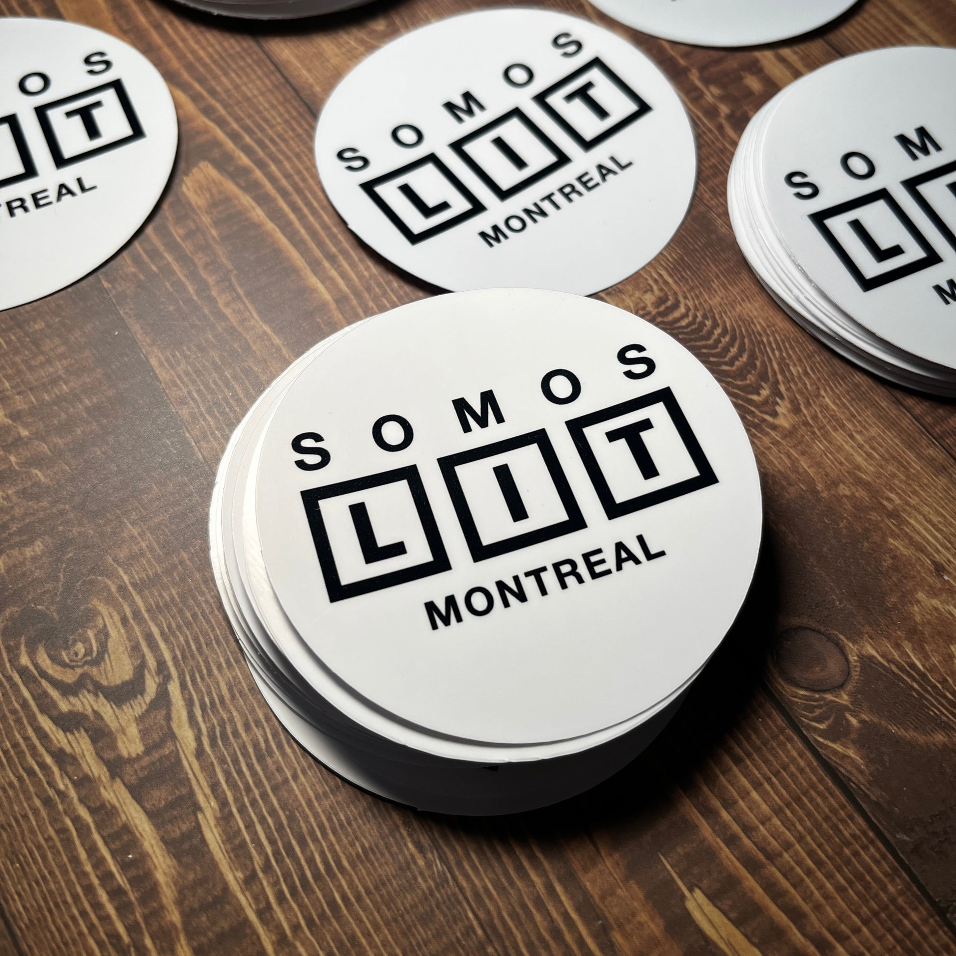 Circular stickers with 'SOMOT Montreal' text on a wooden surface